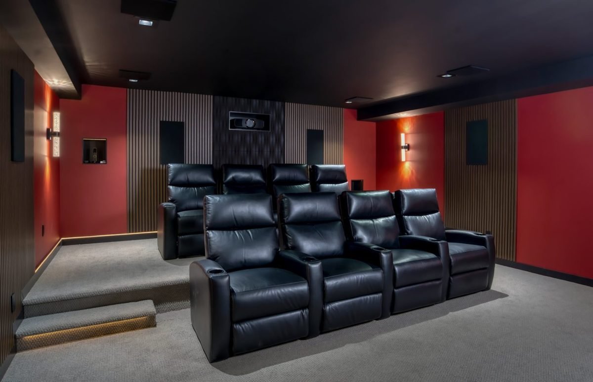 Modern home theater with red walls, wood slat panels and two rows of black recliners